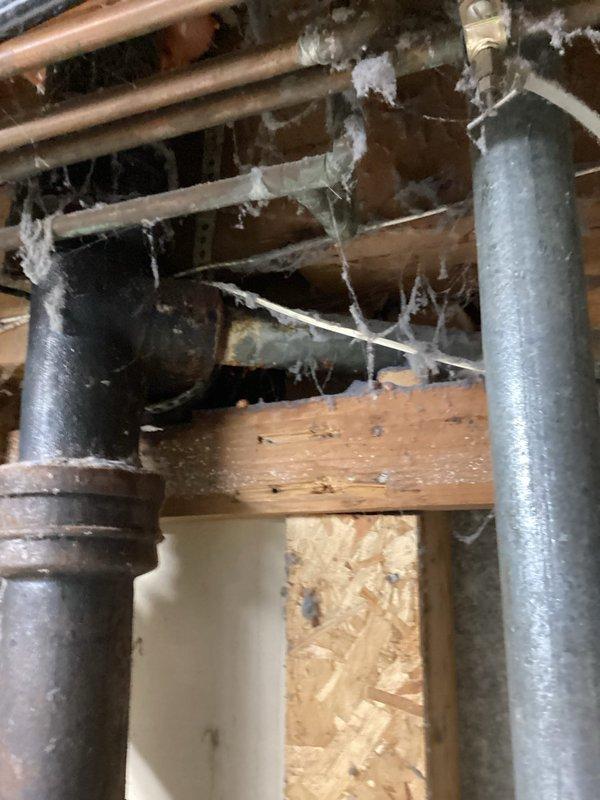 Responded to service call for toilet main pipe replacement. Upon inspection, discovered severely corroded and deteriorated toilet flange with visible rust and mineral deposits. Identified cast iron drain line experiencing internal leaking from upstairs bathroom into basement ceiling below. Documented extensive corrosion on floor drain and compromised drainage system. Due to inaccessible nature of leak and extent of deterioration in cast iron piping system, recommended complete repipe of toilet flange and conversion of cast iron drain line to PVC. Captured photographic documentation showing corroded drain components, water damage staining on surrounding tile surfaces, and exposed basement infrastructure including deteriorated cast iron vertical stack and overhead plumbing lines. Scheduled follow-up assessment for comprehensive quote on toilet flange replacement and full drain line conversion project.