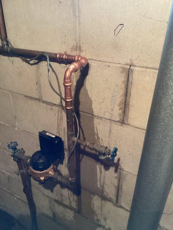 Responded to emergency call for water main leak with significant water flow. Upon arrival, found the main water line leaking at multiple points after the meter, with the existing shut-off valve inoperable and unable to stop water flow. 

Shut off water supply at the meter to contain the leak. Assessed the damaged section of the water main and determined that the compromised piping required replacement rather than repair due to the extent of deterioration. Cut out the failed section of pipe and removed all damaged components.

Installed new copper piping with proper fittings, including new gate valves with operational handles to ensure future shut-off capability. Connected the new section to the existing water main system using appropriate copper elbows, T-connections, and compression fittings. Installed a blue pressure regulator device as part of the new assembly to protect the home's plumbing system.

Restored water service by turning the supply back on at the meter. Tested the entire