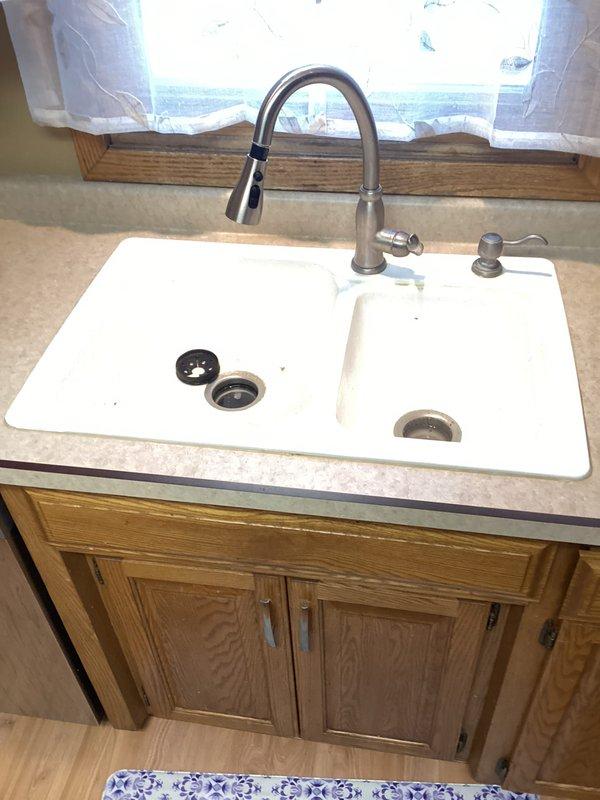 Completed garbage disposal replacement in kitchen under double-basin sink with hardwired electrical connection. Replaced existing disposal unit with new black disposal, ensuring proper mounting and connection to white PVC drain assembly and P-trap configuration. Installation included verifying proper alignment with sink drain opening, securing disposal to mounting ring, and completing straight-wire electrical connection. Provided estimate for potential future work on sink and faucet replacement.