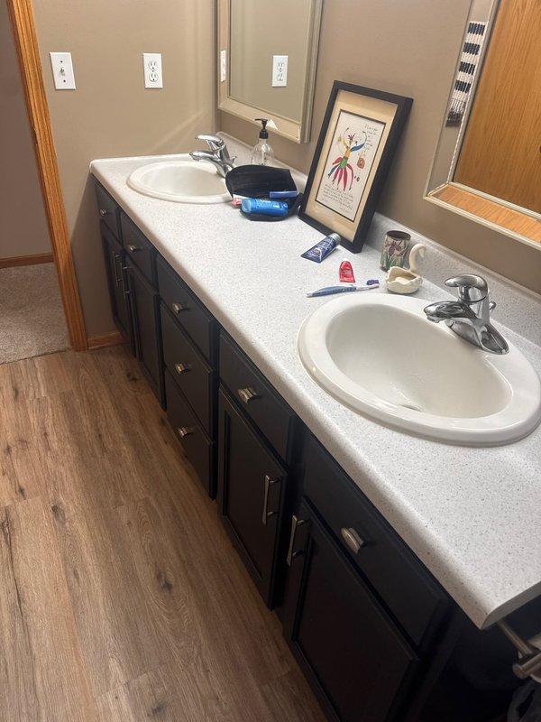 Responded to service call for reported water under carpet and flooring in bathroom. Upon arrival, conducted thorough inspection of bathroom area including vanity, toilet, tub/shower combination, and surrounding flooring. Examined wood-look laminate flooring for moisture damage and investigated potential leak sources. Assessed plumbing fixtures including dual sink vanity with chrome faucets, toilet, and tub/shower plumbing for visible leaks or water intrusion. Determined wet carpet condition was result of ground water infiltration rather than plumbing system failure. No active leaks detected from supply lines, drain lines, or fixture connections. Documented conditions with photographs for service records.