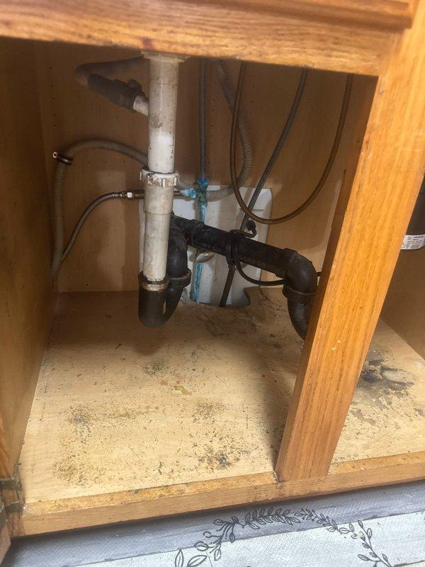 Completed installation of customer-supplied kitchen sink and faucet in existing countertop opening. Installed double-basin stainless steel sink with black faucet and sprayer assembly, connected drain lines with PVC P-trap configuration and white plastic couplings to existing garbage disposal unit, and verified all water supply connections were secure and leak-free.