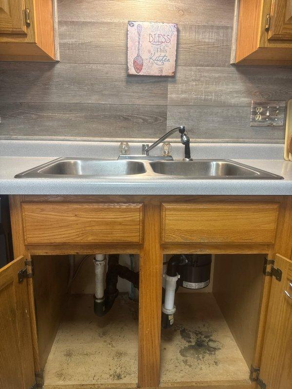 Completed installation of customer-supplied kitchen sink and faucet in existing countertop opening. Installed double-basin stainless steel sink with black faucet and sprayer assembly, connected drain lines with PVC P-trap configuration and white plastic couplings to existing garbage disposal unit, and verified all water supply connections were secure and leak-free.