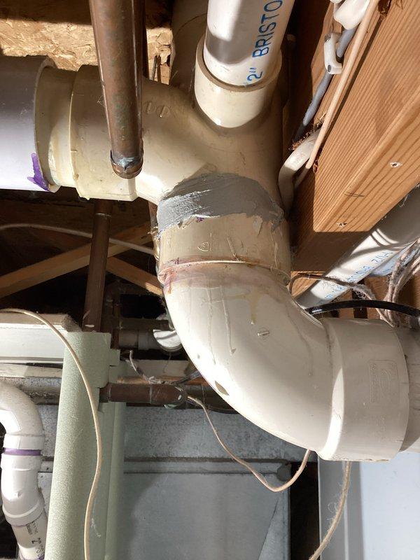 Inspection revealed a cracked 3-inch PVC drainage fitting near the hub connection in the shower/tub drainage system, causing an active leak in the crawl space area. Documented the damage with photographs showing the compromised P-trap assembly and surrounding plumbing infrastructure for insurance claim purposes, with repair scope requiring formal bid due to the extent of work needed.