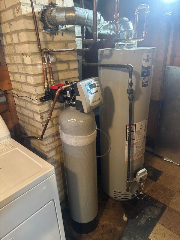 Responded to service call for leaking water softener system. Upon arrival, assessed the utility room and confirmed active leak from the water softener unit. Replaced the failed water softener with new unit, installing beige cylindrical softener tank with black base and white digital control valve system. Installed new Bradford White tanked water heater to replace existing unit. Connected expansion tank to water heater using proper valve assembly with manual shutoff capability. Completed all copper and galvanized pipe connections between water softener, control unit, and water heater with appropriate shut-off valves and fittings throughout the system. Verified all plumbing connections for proper operation and tested system to ensure no leaks present. Left installation clean and fully operational with all equipment functioning as designed.