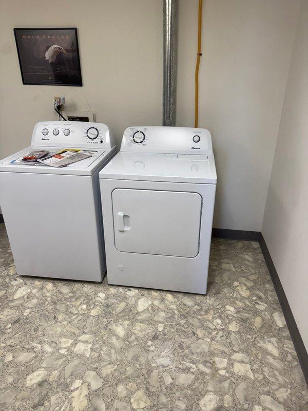 Completed return appointment for gas dryer installation, connecting yellow flexible gas line to wall-mounted shut-off valve and positioning white front-loading dryer unit next to existing washing machine. Verified all gas connections were secure and tested system for proper operation and safety compliance.