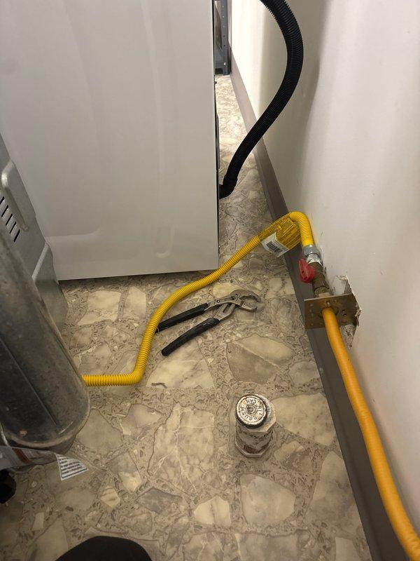 Completed return appointment for gas dryer installation, connecting yellow flexible gas line to wall-mounted shut-off valve and positioning white front-loading dryer unit next to existing washing machine. Verified all gas connections were secure and tested system for proper operation and safety compliance.