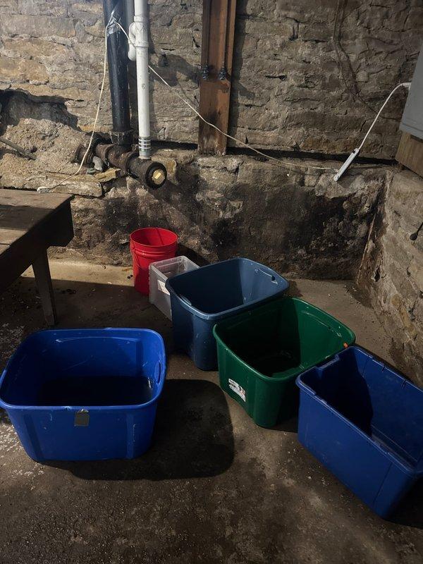 Responded to emergency call for water intrusion in basement with unknown source. Upon arrival, identified active leak in cast iron drain system with visible deterioration and signs of mainline blockage. Basement showed evidence of moisture damage to foundation walls, with multiple collection buckets positioned to catch dripping water from overhead plumbing. Inspected black pipe and associated drain infrastructure, noting extensive corrosion and compromised integrity of cast iron drainage system. Assessed bathroom plumbing connections on upper level where aging fixtures and drain lines connected to deteriorating basement system. Documented condition of failed piping and water damage throughout affected areas. Recommended complete replacement of compromised cast iron drain system due to severity of leaks and blockage issues. Collected standard service call fee and provided customer with assessment findings and replacement options to restore proper drainage function and prevent further wa
