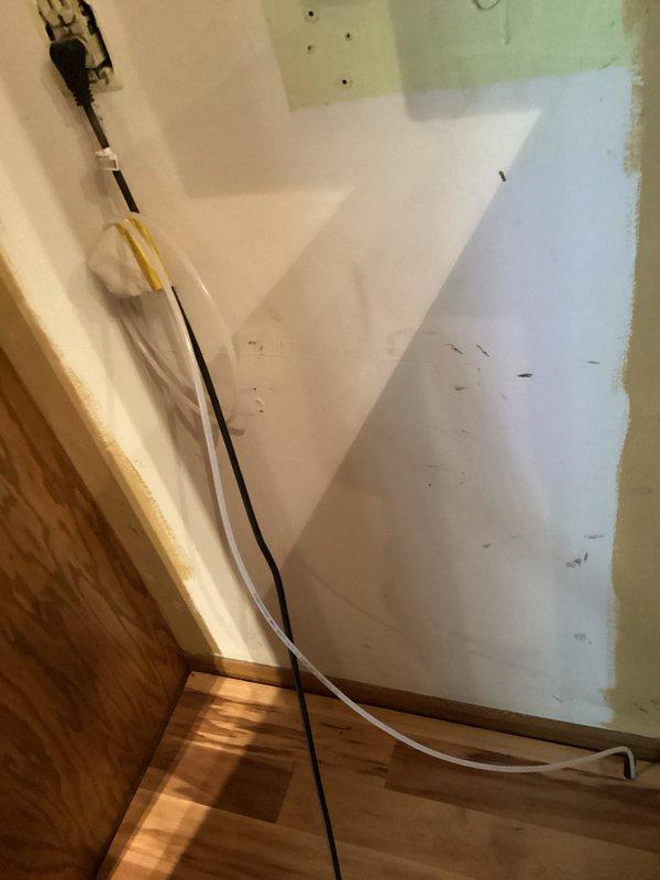 Replaced defective refrigerator water supply line with new line to restore proper water flow to the appliance. Installation completed in unfinished interior space with exposed wiring and construction materials present.