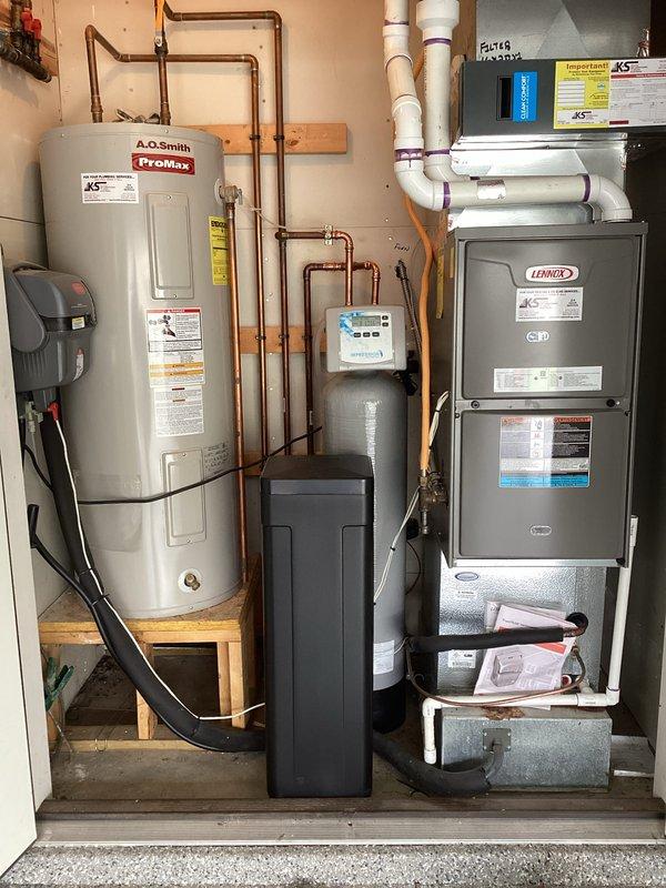 Completed installation of two-piece water softener system with custom-ordered smaller capacity brine tank to accommodate space constraints in residential utility area. Unit was professionally integrated with existing plumbing infrastructure using copper piping connections, positioned centrally between water heater and HVAC furnace, with digital control panel mounted and operational.