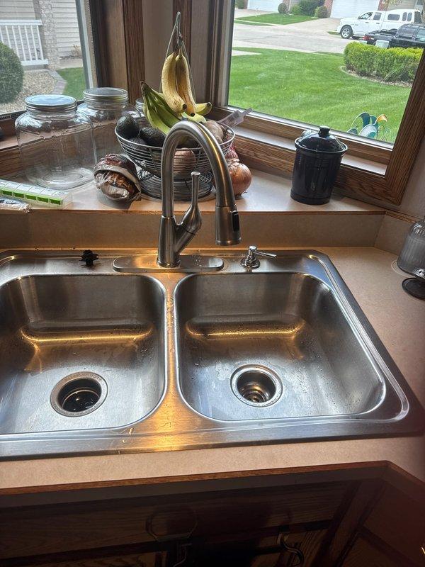 Completed faucet replacement at kitchen sink location. Removed existing faucet assembly, installed new pull-down style faucet fixture, and verified proper connection of hot and cold water supply lines to angle stop valves beneath sink. All connections tested and confirmed leak-free with full water pressure restored to both basins.