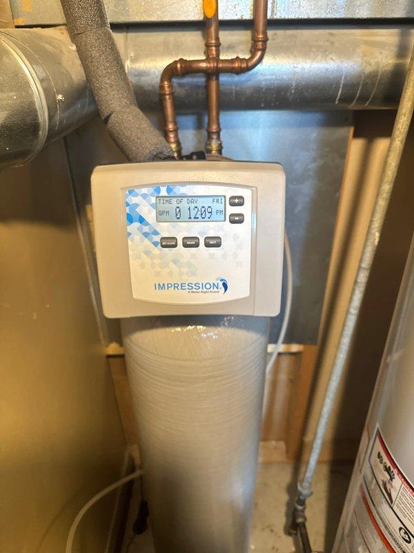 Responded to service call for water softener system reported as not working properly. Upon arrival, performed diagnostic inspection of the Impression brand water softener unit and control panel. Verified system operation, checked digital display showing proper time-of-day settings, inspected plumbing connections including copper piping and brass fittings, and confirmed water softener is functioning correctly. System restored to normal working condition.