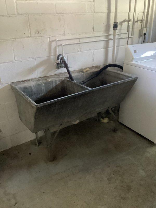Responded to slow-draining laundry tub in basement utility area. Upon inspection, identified aged concrete double-basin sink with internal deterioration causing drainage issues. Washing machine discharge flows into slop sink which is not draining properly due to compromised condition of cement fixture. Recommended removal of existing laundry tub and installation of single standpipe for washing machine connection as permanent solution. Provided estimate for drain clearing attempt, noting that underlying issue stems from deteriorated sink structure rather than main drain line blockage.