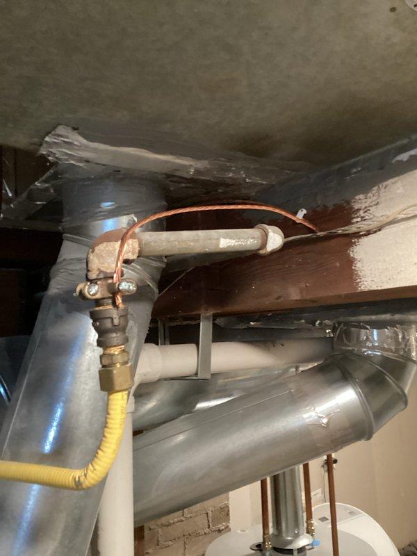Completed CSST bonding installation in accordance with safety codes. Located yellow flexible corrugated stainless steel tubing (CSST) gas line connected to water heater system in basement utility area. Installed proper electrical bonding jumper from CSST gas piping system to electrical grounding system at main panel to protect against lightning strikes and electrical faults. Verified all connections were secure and met code requirements for gas line bonding.