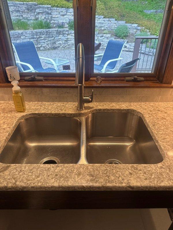 Completed installation of customer-supplied brushed stainless steel kitchen faucet with pull-down sprayer head on double-basin undermount sink. Verified proper water supply connections, tested faucet operation and spray function, and confirmed no leaks in the system.