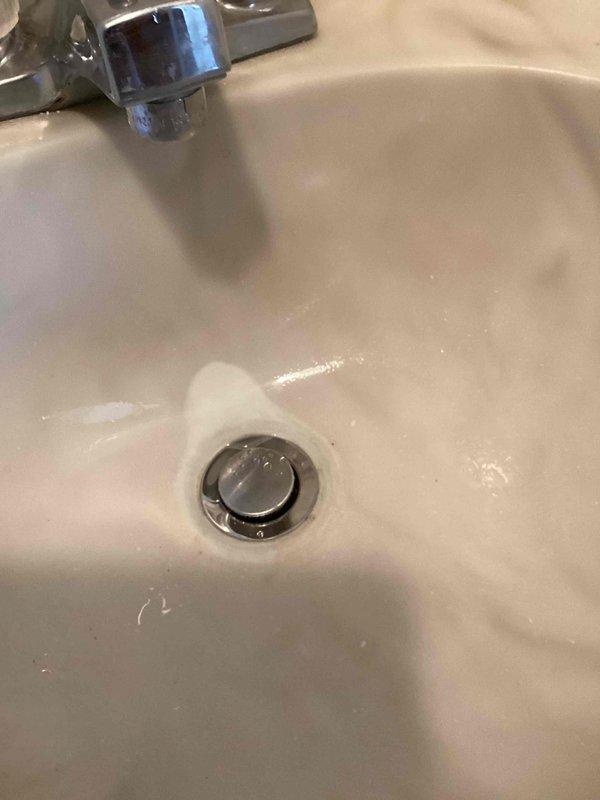 Responded to a water leak at a main floor hallway bathroom lavatory sink. Upon inspection, discovered the pop-up drain assembly and P-trap were deteriorated, cracked, and actively leaking beneath the vanity. Removed the failed pop-up assembly and P-trap drain components. Installed new pop-up drain assembly and P-trap, ensuring proper threaded connections and secure fittings. Tested the system by running the faucet to verify complete water flow and confirmed all connections were leak-free with no drainage issues.