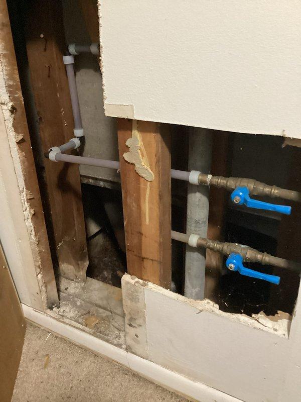 Responded to service call regarding reported drum trap and potential leak in older building. Upon arrival, performed thorough inspection of plumbing system behind wall access opening. Customer initially believed property had drum trap requiring assessment, but inspection revealed standard PVC trap configuration instead. Examined all visible plumbing components including white PVC drainage pipes, copper supply lines, and shut-off valves with blue handles. Inspected P-trap assembly beneath sink fixture and tested all connections for moisture or active leaks. No leaks detected in drainage system or supply lines. Confirmed all plumbing connections were secure and functioning properly with no water intrusion present.