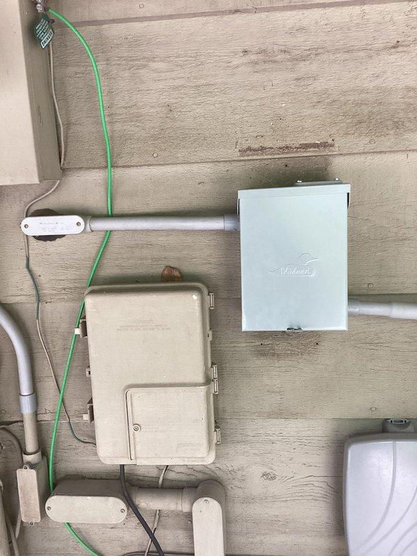 Responded to service call for hot tub disconnect installation at residential property. Removed existing weathered spa disconnect box and replaced with new white exterior-rated disconnect enclosure mounted on exterior wall siding. Installation included proper conduit connections, grounding wire continuity, and secure mounting to building exterior. New disconnect provides code-compliant shutoff for spa equipment and integrates with existing electrical service panel visible in basement utility area.