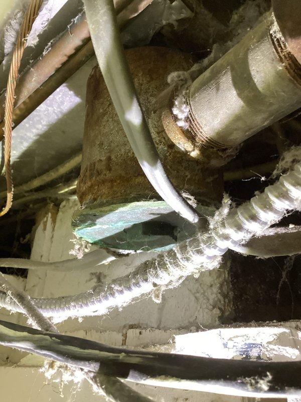 Responded to service call for drum trap replacement on bathtub drainage system. Upon inspection, found heavily corroded drum trap with significant rust deterioration and mineral buildup in confined space adjacent to HVAC ductwork. Previous jetter cleaning service had cleared the blockage but recommended permanent replacement with modern P-trap configuration. Assessed extremely limited access conditions due to proximity of air conditioning duct, which may require relocation for proper drum trap removal. Documented existing conditions showing advanced corrosion on trap body and mineral deposits on connecting pipes. Provided estimate for complete drum trap removal and new P-trap installation to upgrade drainage system to current plumbing standards and prevent future blockages.