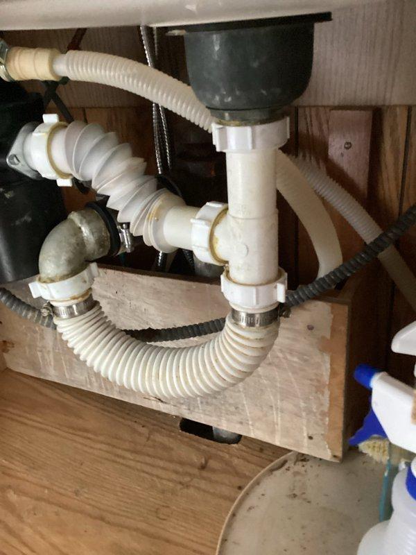Responded to kitchen sink leak caused by improperly installed drainage system. Upon inspection, found accordion-style drain assembly and P-trap connections leaking due to incorrect installation of all under-sink plumbing components. Removed existing drainage system and garbage disposal unit, then completely reworked the drain configuration, relocating the garbage disposal to the opposite sink basin. Installed new PVC P-trap assembly with proper connections, secured all flexible drain hoses with appropriate clamps, and verified all joints were sealed correctly. Tested system by running water through both sink basins and garbage disposal, confirming no leaks and proper drainage flow throughout the entire assembly.