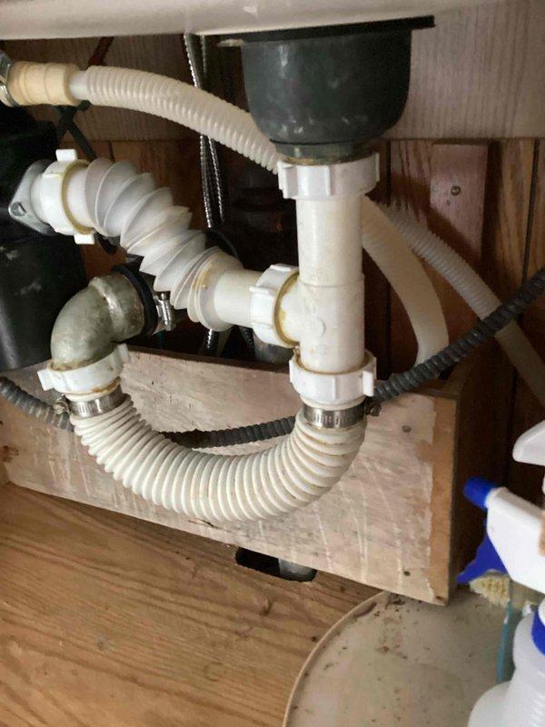 Responded to kitchen sink leak caused by improperly installed drainage system. Upon inspection, found accordion-style drain assembly and P-trap connections leaking due to incorrect installation of all under-sink plumbing components. Removed existing drainage system and garbage disposal unit, then completely reworked the drain configuration, relocating the garbage disposal to the opposite sink basin. Installed new PVC P-trap assembly with proper connections, secured all flexible drain hoses with appropriate clamps, and verified all joints were sealed correctly. Tested system by running water through both sink basins and garbage disposal, confirming no leaks and proper drainage flow throughout the entire assembly.