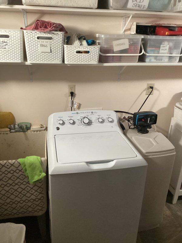 Completed installation of water softener system in residential laundry room. Unit was mounted and positioned on top of washing machine, connected to existing plumbing lines, and powered through nearby electrical outlet. System was tested and verified operational upon completion.