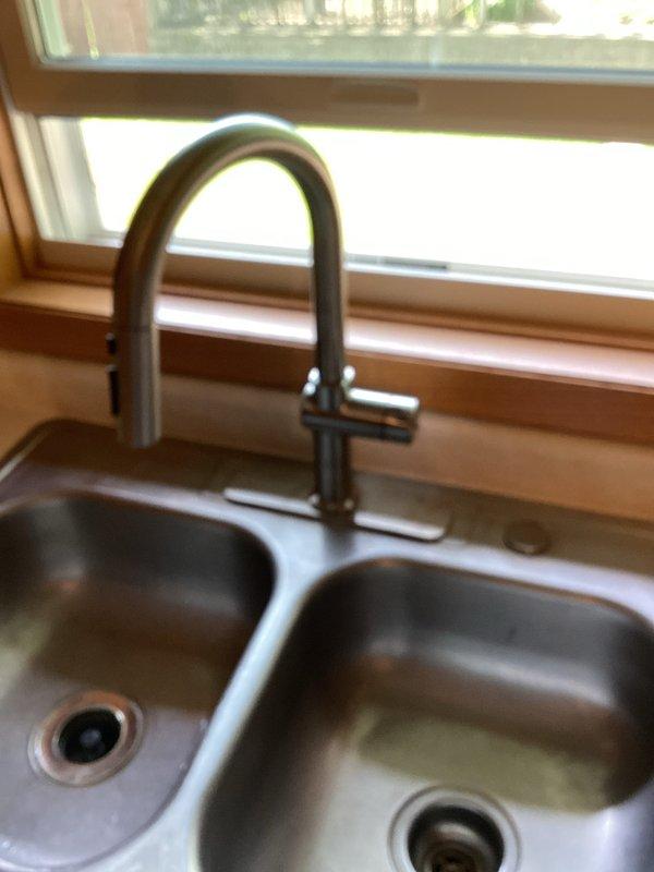 Removed existing kitchen faucet from double-basin stainless steel sink and installed new customer-supplied pull-down faucet with brushed nickel finish. Completed all plumbing connections, verified proper water flow and temperature control operation, and tested spray head functionality. All fixtures operating correctly with no leaks detected upon final inspection.