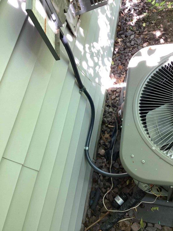 Returned to site to address AC whip concerns and installed new electrical whip assembly connecting the outdoor condensing unit to the building's electrical system. The new flexible conduit was properly secured to the light green vinyl siding and routed to the beige air conditioning unit positioned on the concrete pad, ensuring code-compliant electrical connection for the HVAC equipment.