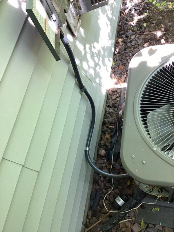 Returned to site to address AC whip concerns and installed new electrical whip assembly connecting the outdoor condensing unit to the building's electrical system. The new flexible conduit was properly secured to the light green vinyl siding and routed to the beige air conditioning unit positioned on the concrete pad, ensuring code-compliant electrical connection for the HVAC equipment.