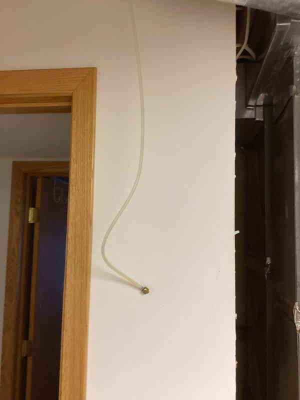Responded to a water leak emergency involving a damaged 1/4" refrigerator supply line running from the mechanical room to an upstairs kitchen. Upon arrival, identified multiple pinhole leaks, cracks, and breaks in the plastic supply tubing routed through the ceiling joists. Immediately shut off the needle valve at the source in the mechanical room to stop active water flow and prevent further damage. Disconnected the compromised supply line from the valve to isolate the system. The faulty supply line will require complete replacement from the mechanical room shutoff valve to the refrigerator connection point. Documented existing plumbing infrastructure including copper water lines and HVAC ductwork in the exposed ceiling area for reference during future repair work.
