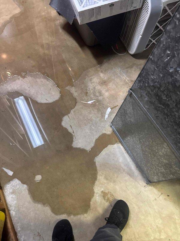 Responded to no cooling complaint and found AC system not maintaining temperature. Diagnosed low refrigerant charge caused by leak at condenser coil. Upon inspection of indoor unit, discovered significant water damage to floor from failed evaporator coil drain pan with visible hole causing condensate overflow. Documented extensive flooding in mechanical room with standing water throughout area. Provided repair estimate for refrigerant leak repair and drain pan replacement, and scheduled project manager visit for full system replacement evaluation due to multiple component failures.