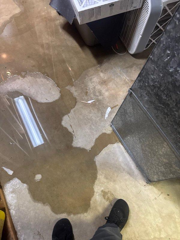 Responded to no cooling complaint and found AC system not maintaining temperature. Diagnosed low refrigerant charge caused by leak at condenser coil. Upon inspection of indoor unit, discovered significant water damage to floor from failed evaporator coil drain pan with visible hole causing condensate overflow. Documented extensive flooding in mechanical room with standing water throughout area. Provided repair estimate for refrigerant leak repair and drain pan replacement, and scheduled project manager visit for full system replacement evaluation due to multiple component failures.