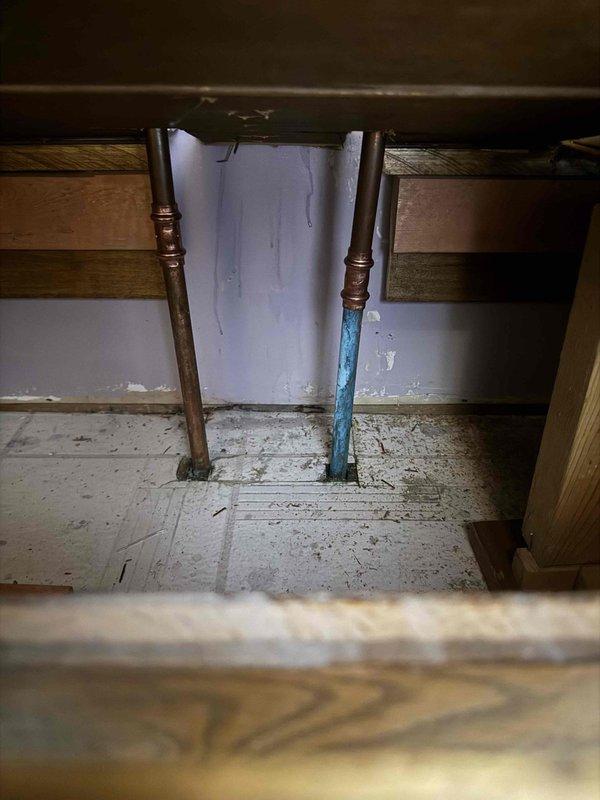 Responded to emergency call for water leak affecting bathroom wall and ceiling, initially reported after AC activation. Upon investigation, identified leak source as lavatory supply lines compromised during recent remodeling work. Replaced damaged section of 1/2" copper fittings and associated connections to eliminate leak. Documented repair work with photographs showing access point through floor opening and surrounding plumbing infrastructure.