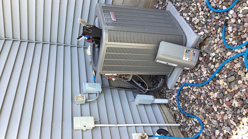 Responded to service call for loud fan noise on residential AC unit. Upon inspection, identified loose side panel causing vibration and rattling sounds. Secured panel and discovered unit was low on refrigerant charge. Checked system pressures and confirmed refrigerant leak present. Documented equipment condition with photos showing outdoor condenser unit installation, surrounding components, and overall system layout. Presented customer with repair options including leak detection/repair with refrigerant recharge versus full system replacement based on age and condition of equipment.