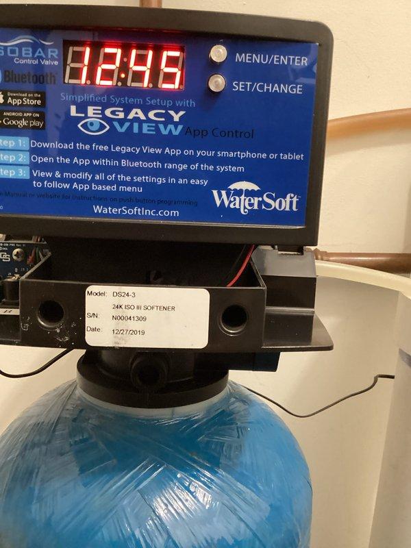 Responded to service call for malfunctioning WaterSoft Legacy View water softener system (Model DS24-3, 24K ISO III). Upon inspection, discovered brine tank was full of water, indicating regeneration cycle failure. Diagnosed control valve malfunction preventing proper brine draw and backwash cycles. Documented system specifications and photographed control head display readings and installation configuration for parts ordering purposes. Customer will obtain replacement parts directly through WaterSoft company, and technician will return for installation upon parts arrival.