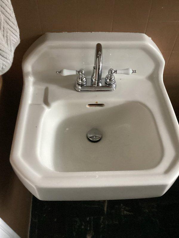 Returned to property to complete lavatory faucet installation in bathroom. Successfully installed white porcelain wall-mounted sink with chrome two-handle faucet featuring traditional cross-handle design. Connected all supply lines and drain assembly, including P-trap installation with proper venting to prevent sewer gas infiltration. Verified proper water flow, tested both hot and cold water handles for functionality, and confirmed pop-up drain stopper operation. All plumbing connections secured and leak-tested to ensure system integrity.