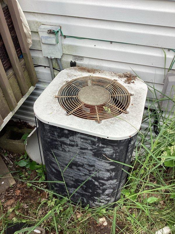 Responded to no cooling call on aging outdoor condensing unit. Upon arrival, found AC fan motor not operating. Inspection revealed burnt electrical wiring, failed condenser fan motor, and damaged condenser coils with significant debris accumulation. Unit accessibility severely compromised due to ground settling, causing equipment to be positioned directly against building structure with inadequate clearance for proper service or airflow. Heavy vegetation growth around base and extensive dirt/debris buildup on top panel indicate lack of routine maintenance. 

Replaced condenser fan motor and repaired burnt wiring to restore immediate operation. However, due to damaged coils and critical positioning issues from settling, unit serviceability remains compromised long-term. Recommended obtaining pricing for relocating equipment away from structure to meet manufacturer clearance specifications and allow proper maintenance access. Unit condition and age suggest consideration for replacement m