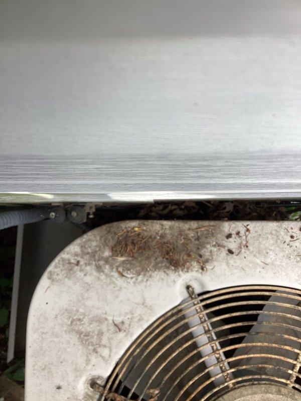 Responded to no cooling call on aging outdoor condensing unit. Upon arrival, found AC fan motor not operating. Inspection revealed burnt electrical wiring, failed condenser fan motor, and damaged condenser coils with significant debris accumulation. Unit accessibility severely compromised due to ground settling, causing equipment to be positioned directly against building structure with inadequate clearance for proper service or airflow. Heavy vegetation growth around base and extensive dirt/debris buildup on top panel indicate lack of routine maintenance. 

Replaced condenser fan motor and repaired burnt wiring to restore immediate operation. However, due to damaged coils and critical positioning issues from settling, unit serviceability remains compromised long-term. Recommended obtaining pricing for relocating equipment away from structure to meet manufacturer clearance specifications and allow proper maintenance access. Unit condition and age suggest consideration for replacement m