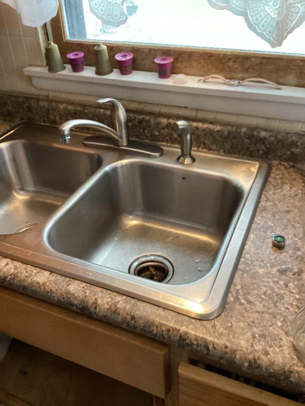 Responded to call regarding dishwasher backing up into sink and leaking around kitchen sink area. Upon inspection, identified leak originating from side sprayer assembly when faucet was in use. Determined that repair was not feasible and complete replacement was necessary. Removed existing kitchen faucet and installed new Moen single-handle faucet with side sprayer, restoring proper function and eliminating all leaks.