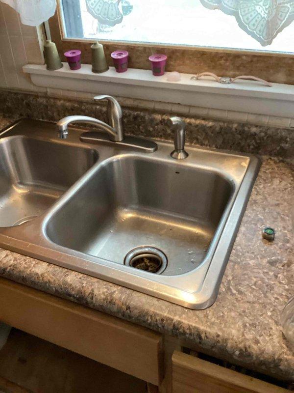 Responded to call regarding dishwasher backing up into sink and leaking around kitchen sink area. Upon inspection, identified leak originating from side sprayer assembly when faucet was in use. Determined that repair was not feasible and complete replacement was necessary. Removed existing kitchen faucet and installed new Moen single-handle faucet with side sprayer, restoring proper function and eliminating all leaks.