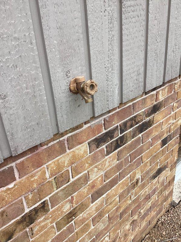 Technician successfully replaced a defective outdoor hose bibb on the building's exterior wall. The old brass fixture was removed from the white siding above the brick foundation, and a new hose bibb was installed in the same location. Water supply was restored to the home and tested to confirm proper operation of the new fixture without leaks.