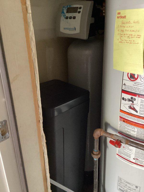 Completed installation of Impression Series two-piece water softener system in utility closet. Mounted wall control unit with digital display above storage tank, connected all necessary plumbing lines, and verified proper system operation alongside existing water heater and HVAC equipment.