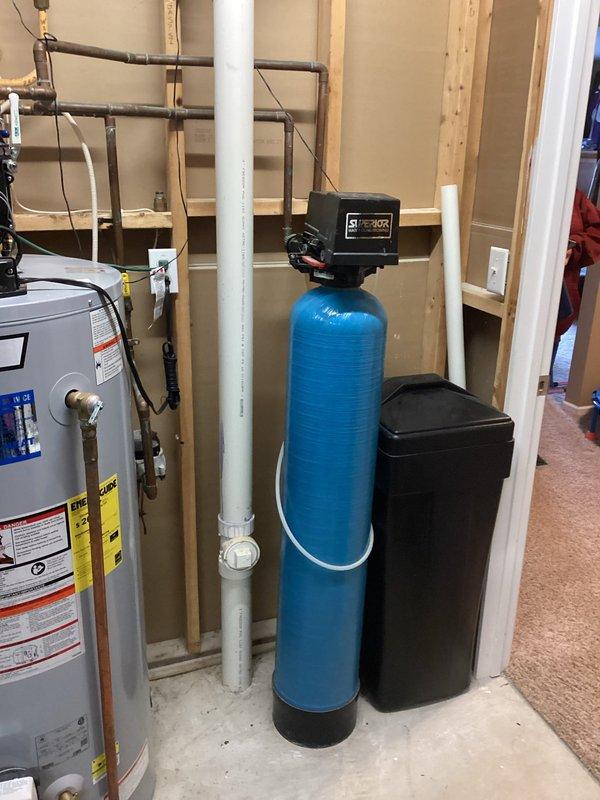 Responded to service call for non-functioning water softener system. Upon inspection, determined the existing water softener unit was inoperable and required full replacement. Successfully removed the failed water softener and installed a new blue cylindrical water softener tank with electronic control head, brine tank, and associated plumbing connections in the utility room. Verified proper operation of the new system and ensured all connections to existing water heater and household plumbing were secure and functioning correctly.
