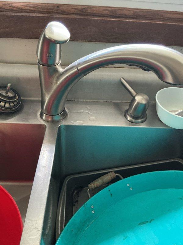 Responded to a kitchen faucet leak that had been occurring over an extended period, causing water damage to penetrate through the countertop and into the basement below. Upon inspection, identified internal faucet failure as the source of the continuous leak. Assessed damage to surrounding areas including countertops, cabinetry, and potential mold growth beneath the sink and in the basement. Documented conditions with photographs showing the affected kitchen sink area with stainless steel basin, single-handle chrome faucet, and under-sink plumbing configuration including P-trap assembly and garbage disposal unit. Noted visible water staining and deterioration on flooring and surfaces beneath the sink. Provided estimate for complete faucet replacement and advised that countertop and cabinet replacement, along with professional mold remediation, would be necessary before proceeding with any additional plumbing work to ensure proper installation and prevent future issues.