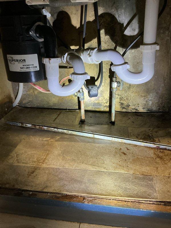 Responded to a kitchen faucet leak that had been occurring over an extended period, causing water damage to penetrate through the countertop and into the basement below. Upon inspection, identified internal faucet failure as the source of the continuous leak. Assessed damage to surrounding areas including countertops, cabinetry, and potential mold growth beneath the sink and in the basement. Documented conditions with photographs showing the affected kitchen sink area with stainless steel basin, single-handle chrome faucet, and under-sink plumbing configuration including P-trap assembly and garbage disposal unit. Noted visible water staining and deterioration on flooring and surfaces beneath the sink. Provided estimate for complete faucet replacement and advised that countertop and cabinet replacement, along with professional mold remediation, would be necessary before proceeding with any additional plumbing work to ensure proper installation and prevent future issues.