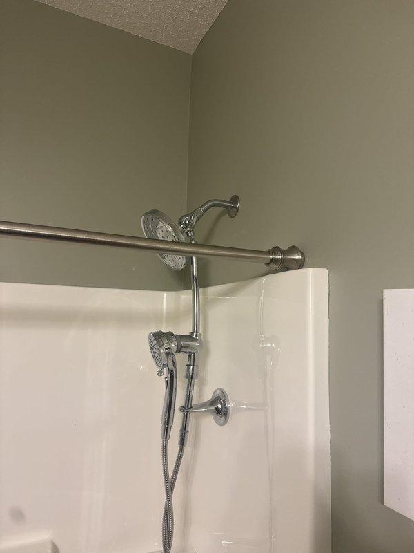 Completed installation of shower slide bars and chrome fixture components in residential bathroom. Installed dual showerhead system including fixed overhead showerhead and handheld shower attachment with flexible hose, along with wall-mounted control valve and chrome curtain rod. All fixtures properly mounted to shower surround and tested for proper operation.