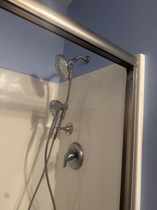 Completed installation of shower slide bars and chrome fixture components in residential bathroom. Installed dual showerhead system including fixed overhead showerhead and handheld shower attachment with flexible hose, along with wall-mounted control valve and chrome curtain rod. All fixtures properly mounted to shower surround and tested for proper operation.
