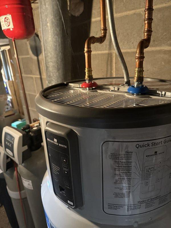 Responded to repeat service call for Bradford White heat pump water heater displaying FF error code related to air system malfunction. Upon inspection, diagnosed seized electronic expansion valve (EEV) preventing proper refrigerant flow through the heat pump system. Documented unit condition and component failure with photographs of internal compartment showing copper refrigerant lines, blower assembly, and electrical connections, as well as external view of unit with control panel and plumbing connections. Determined unit requires warranty replacement due to failed EEV component that cannot be freed or repaired in field conditions.