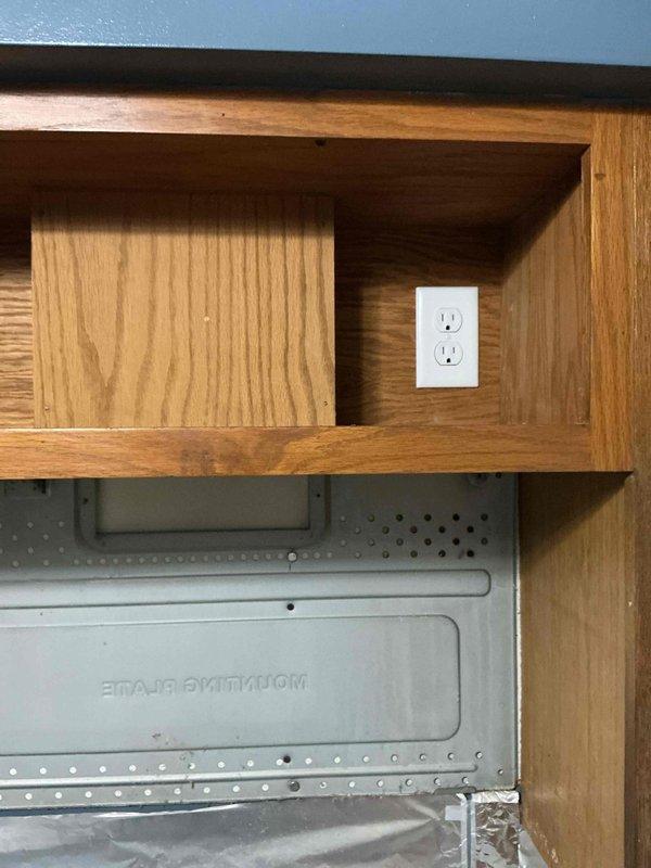 Installed new electrical outlet with cover plate inside cabinet above range to accommodate wall-mounted microwave. Previous microwave was hard-wired; converted to plug-in configuration by adding dedicated receptacle within cabinet compartment. Outlet positioned for proper microwave connection and secured according to electrical code requirements.