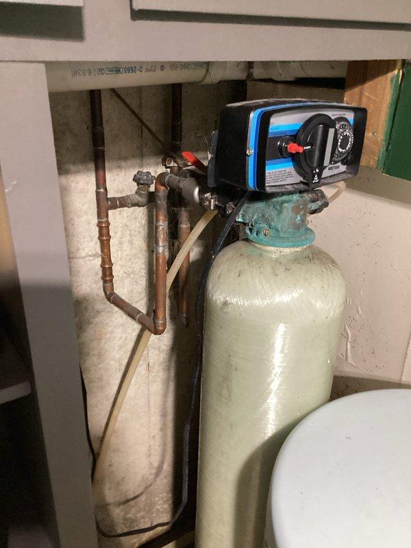 Conducted on-site evaluation of existing water softening system in basement utility room to provide estimate for new water softener installation. Assessed current equipment configuration including tall cylindrical softener tank with control valve assembly, copper plumbing connections, and white brine storage tank. Documented existing system layout, plumbing connections, and installation area to determine replacement requirements and specifications for new water treatment equipment.