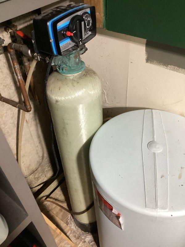 Conducted on-site evaluation of existing water softening system in basement utility room to provide estimate for new water softener installation. Assessed current equipment configuration including tall cylindrical softener tank with control valve assembly, copper plumbing connections, and white brine storage tank. Documented existing system layout, plumbing connections, and installation area to determine replacement requirements and specifications for new water treatment equipment.